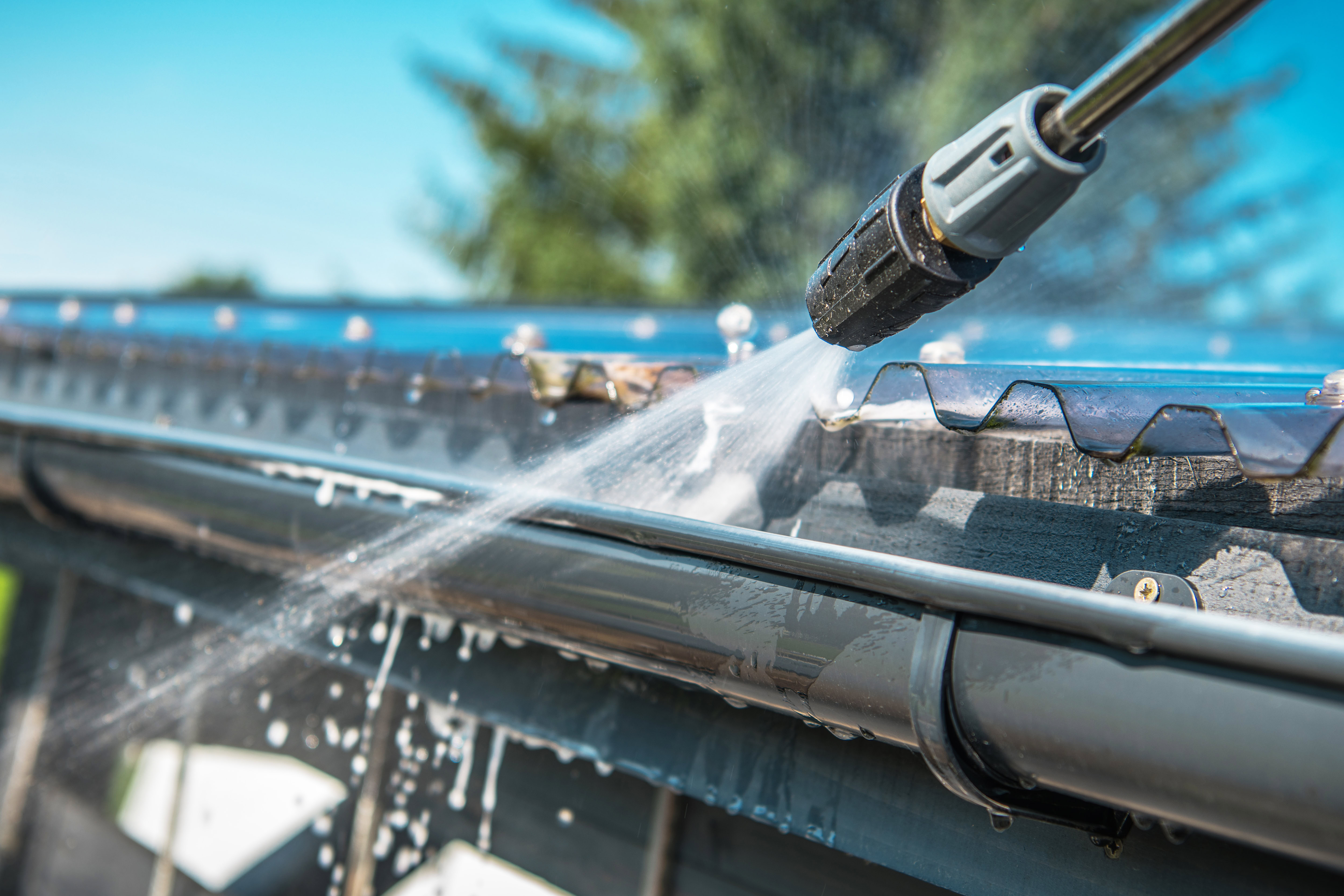 close up picture of a power washer spraying water into a roof gutter
