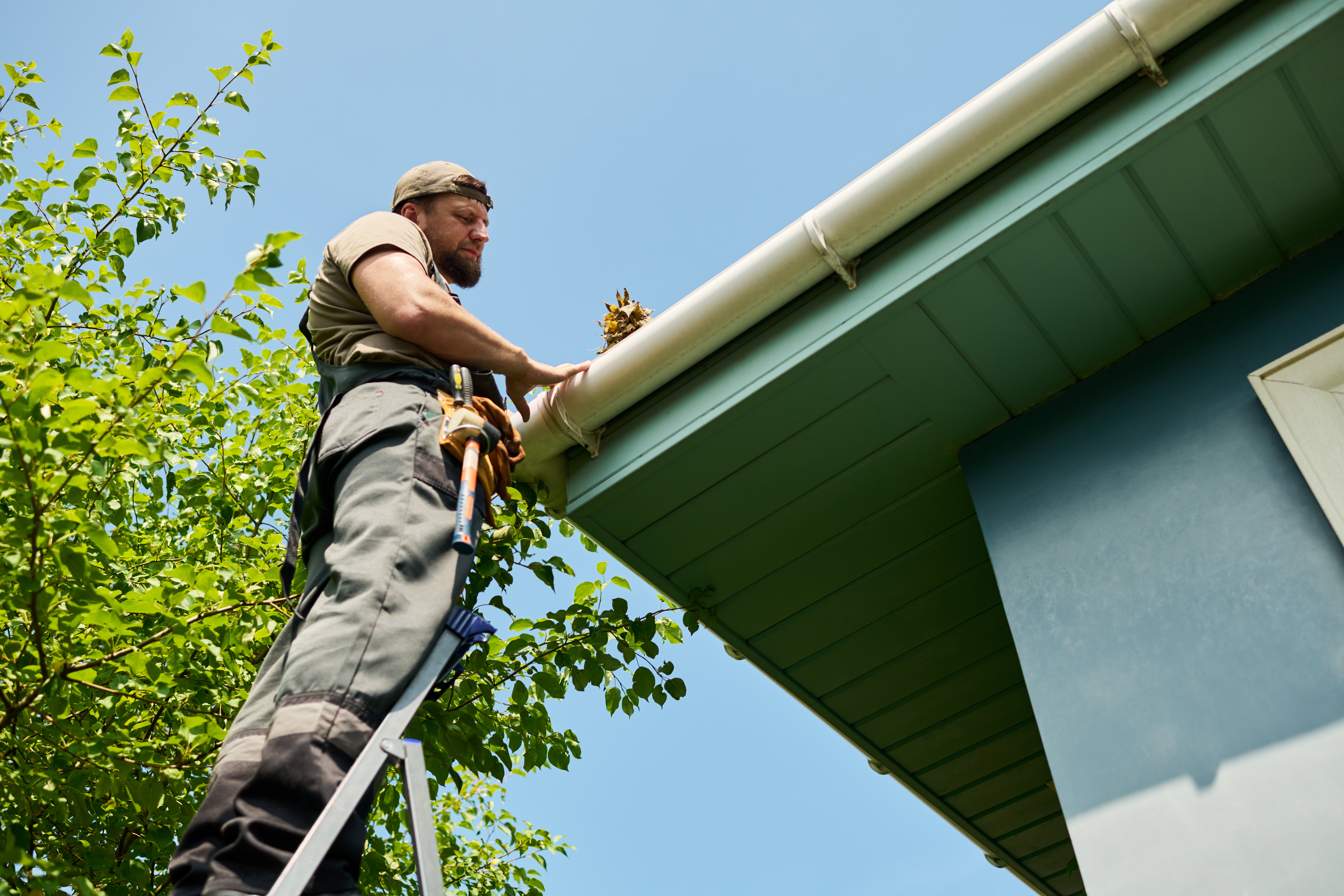 man on a ladder inspecting gutters on a roof | recurring property maintenance program