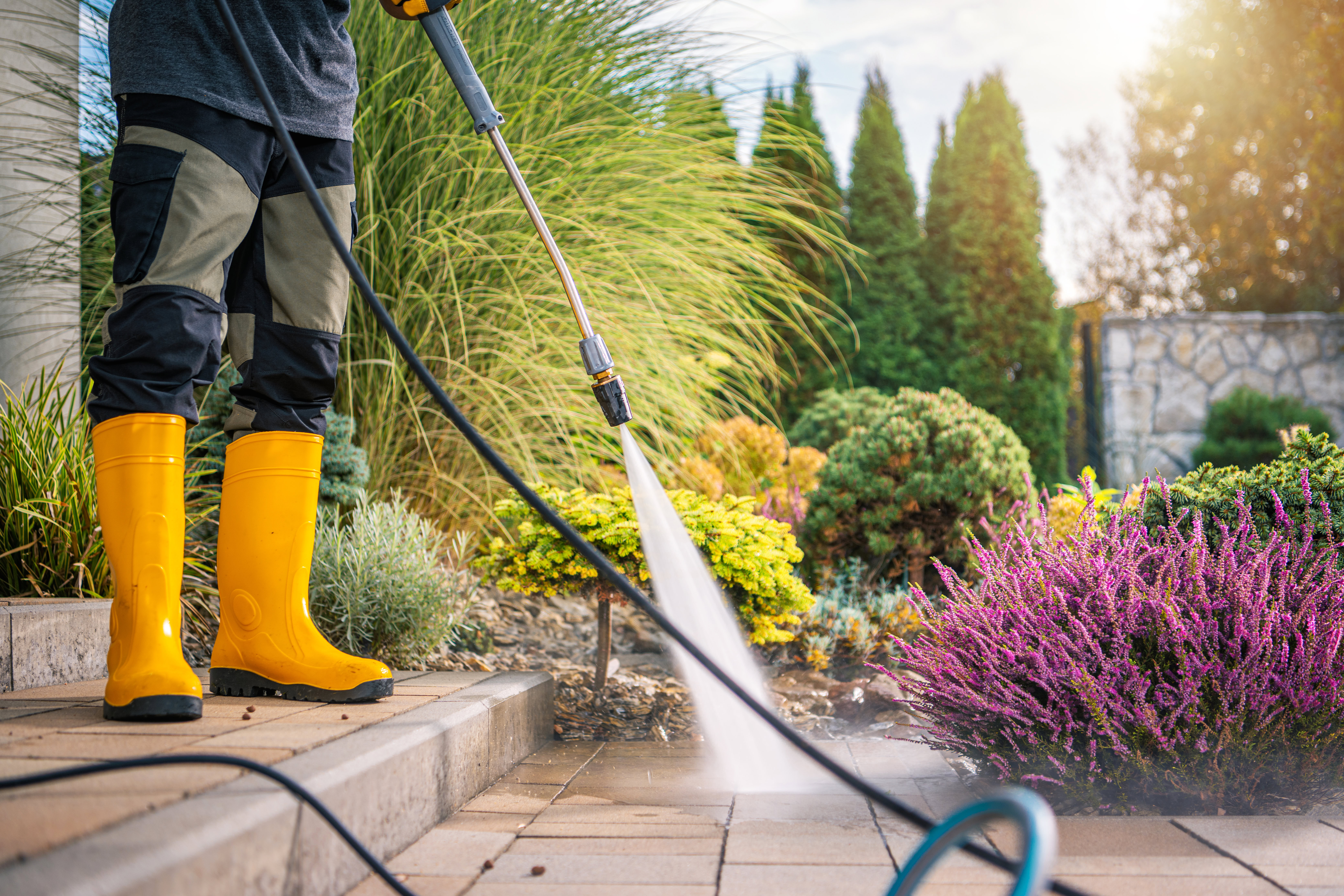 Person wearing yellow boots pressure washing the front of a home