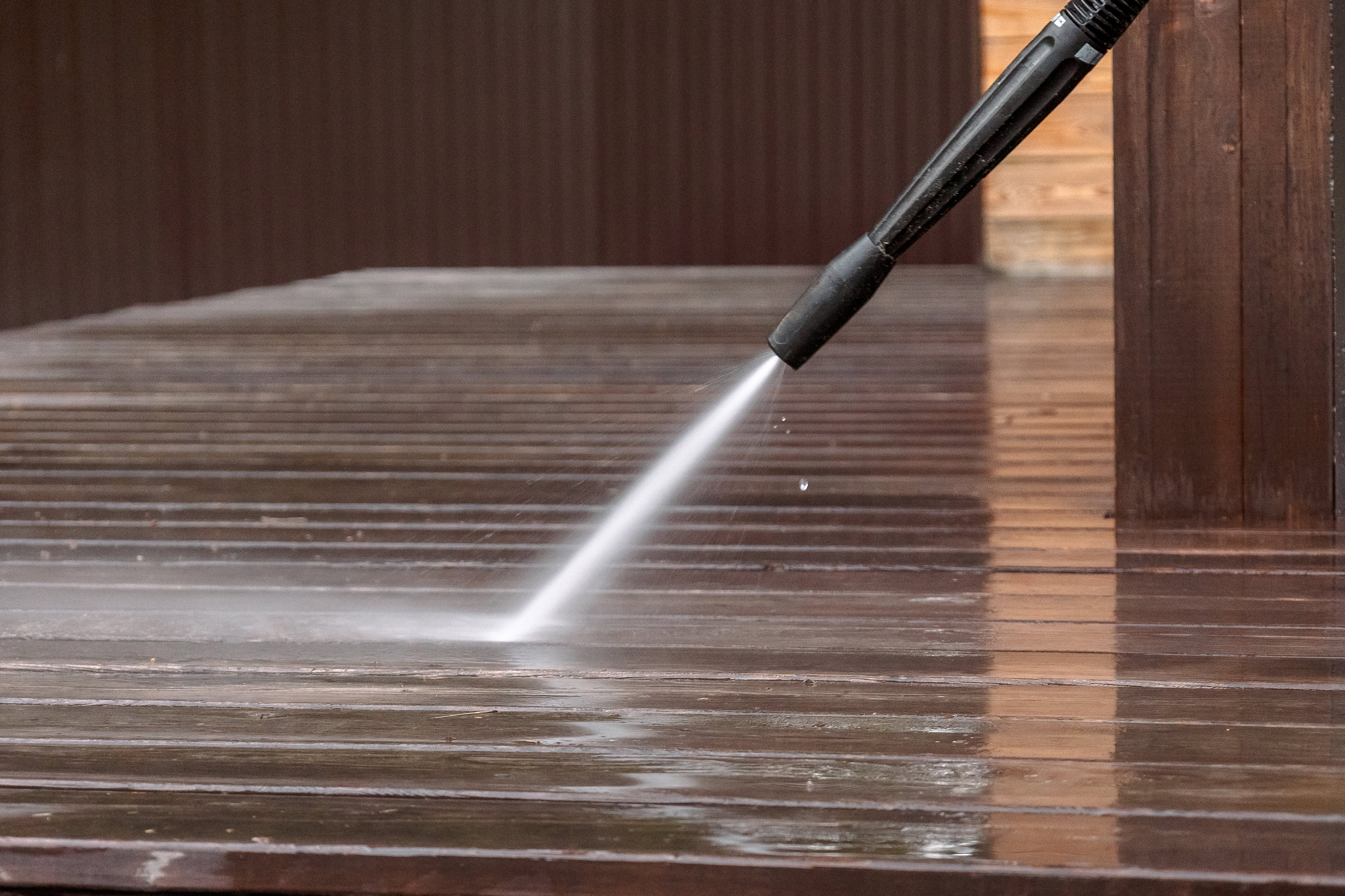 close up picture of a pressure washer spraying water on to a wood deck