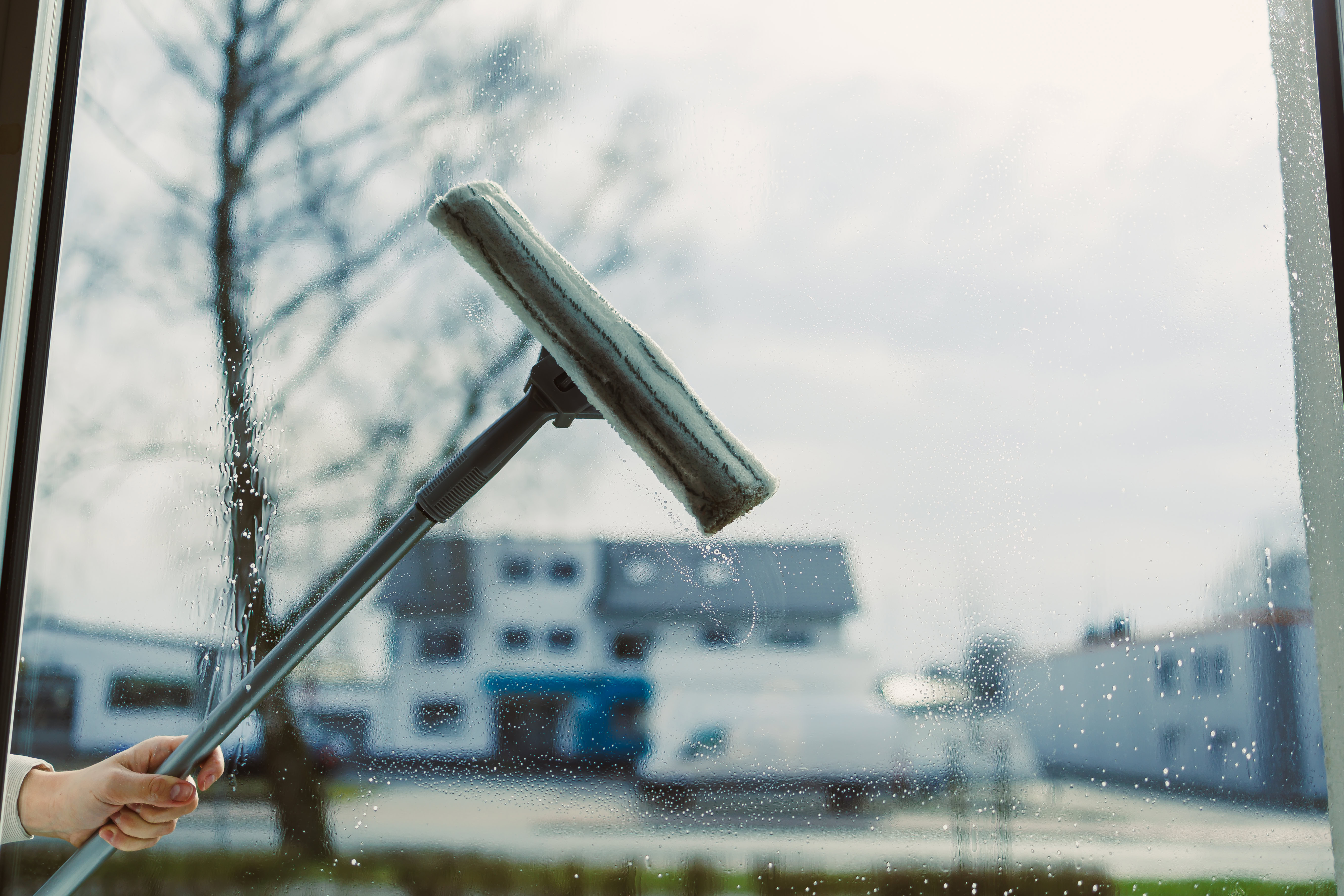 person holding an extended squeegee on the outside of a window | window washing services
